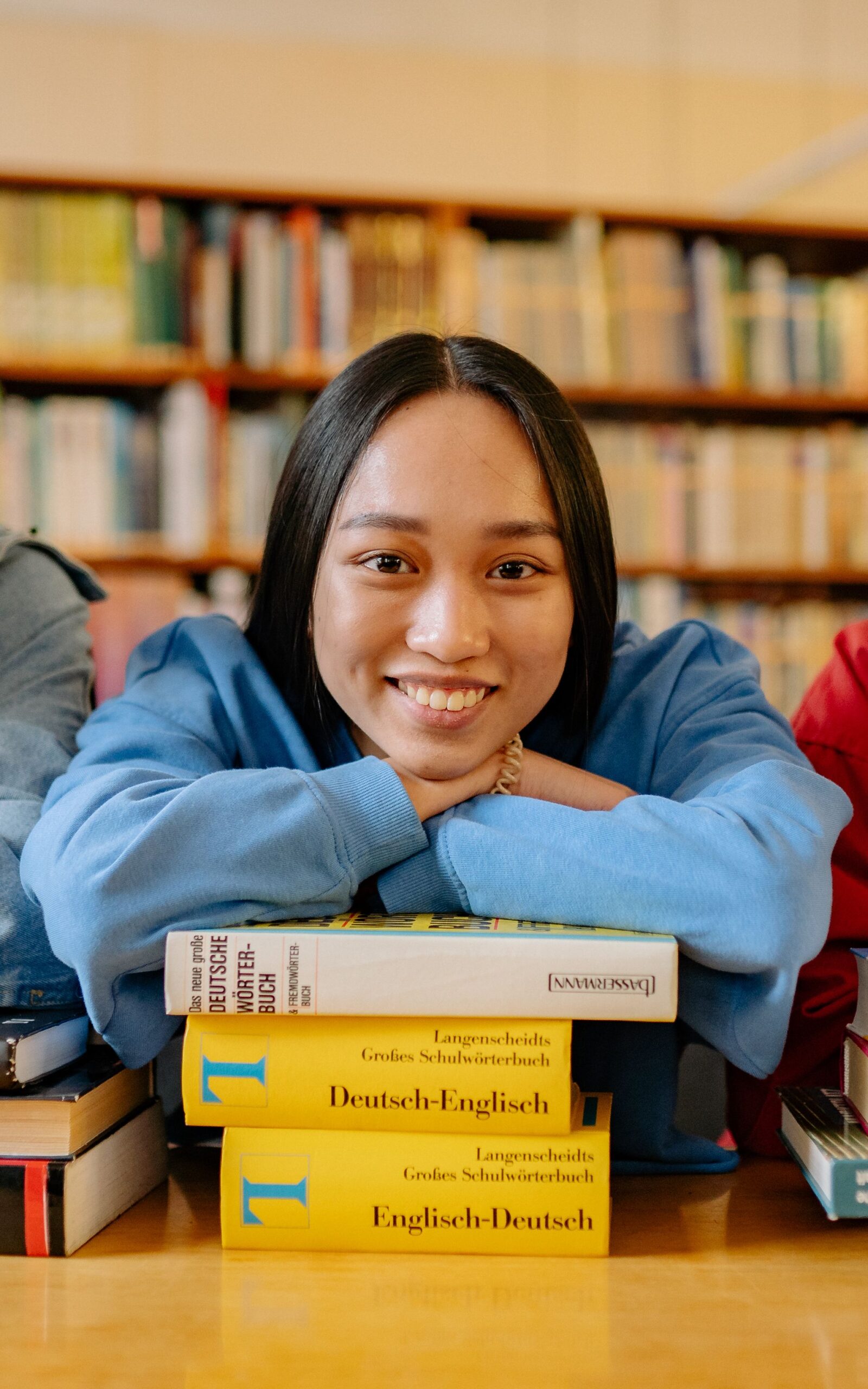 Smiling student leaning on a stack of books in a library