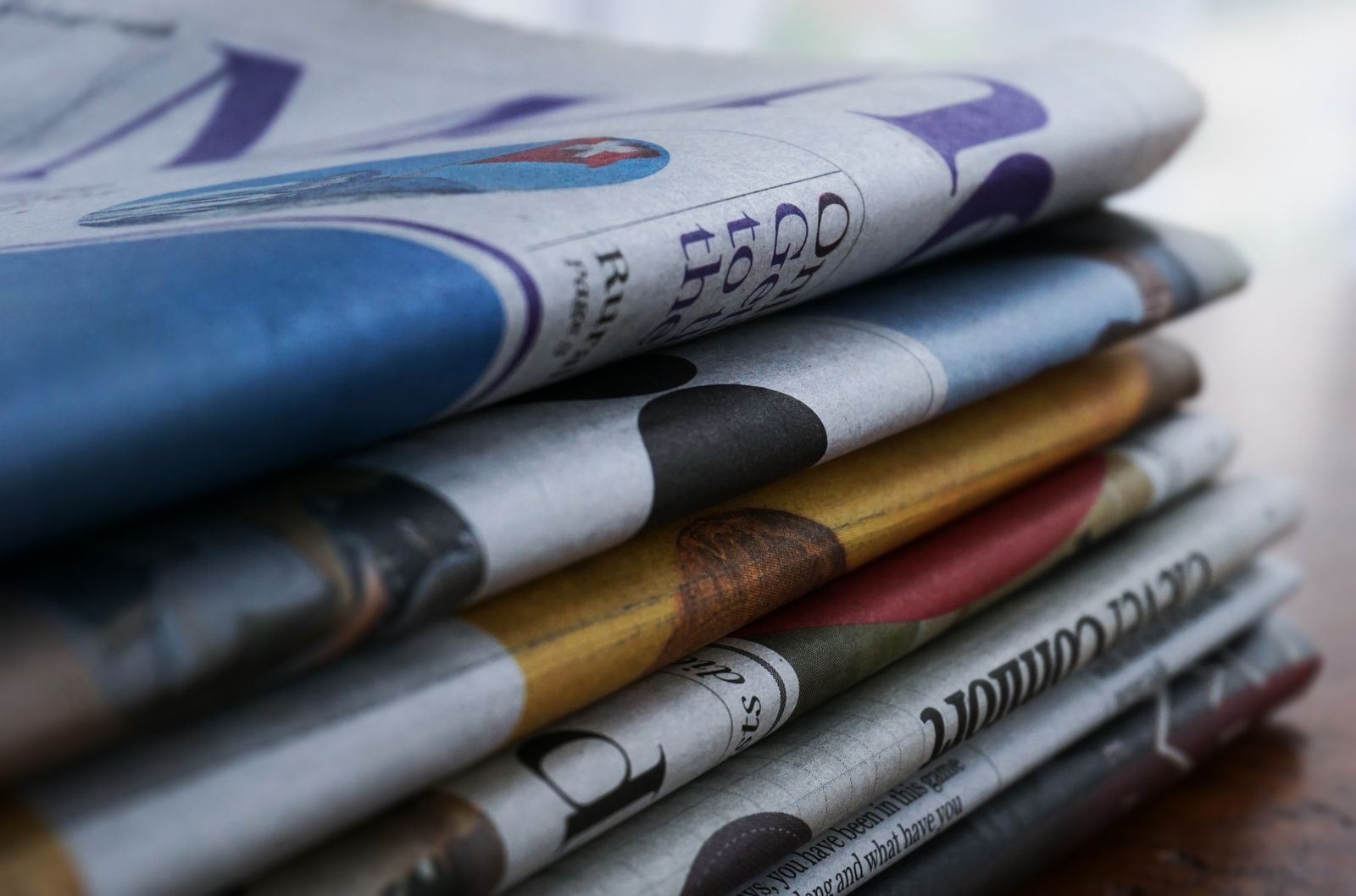Close-up of a stack of colorful newspapers on a wooden table, showcasing print media