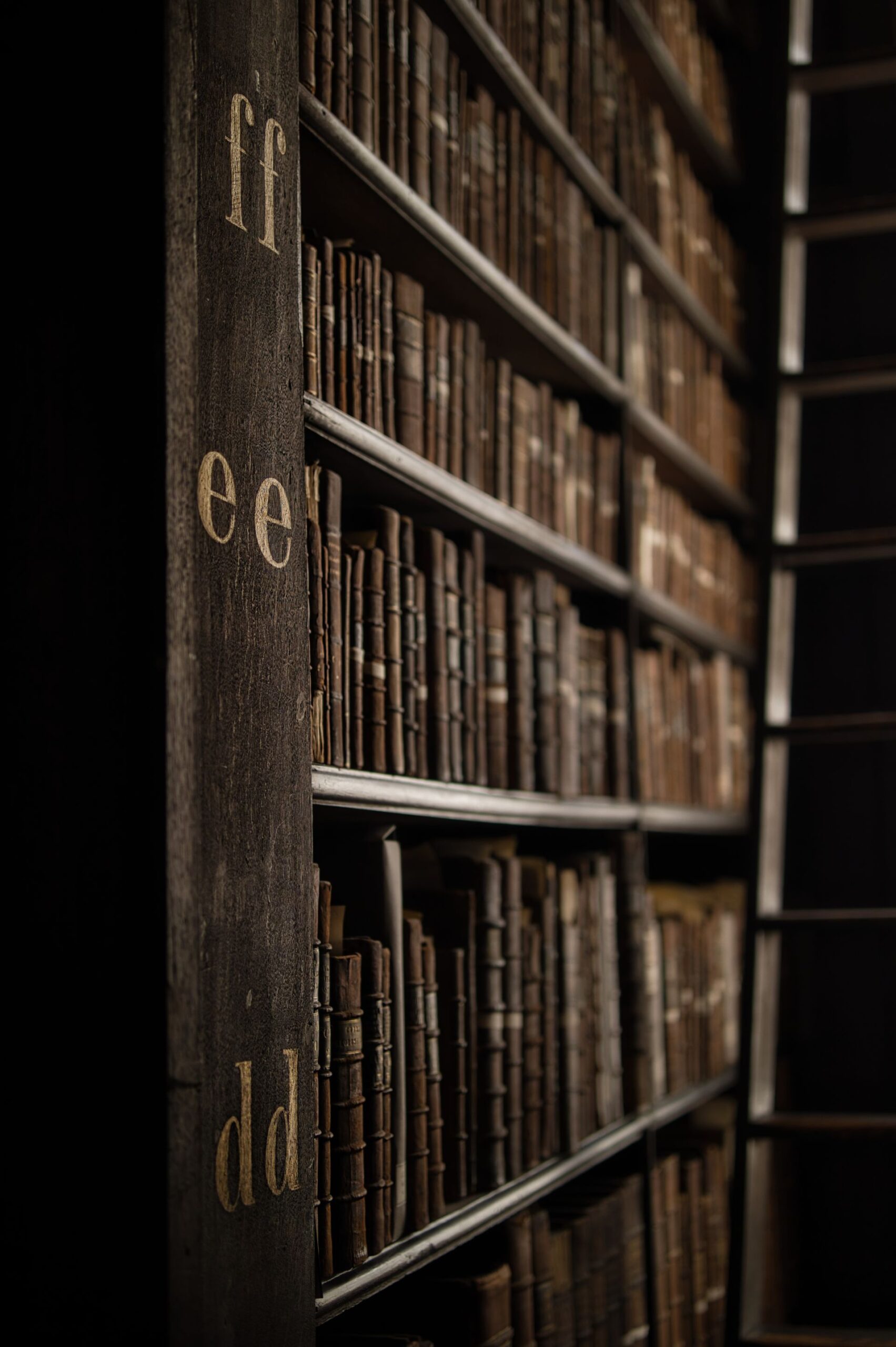 Old books on a wooden bookshelf in a dimly lit library, capturing the historic ambiance.
