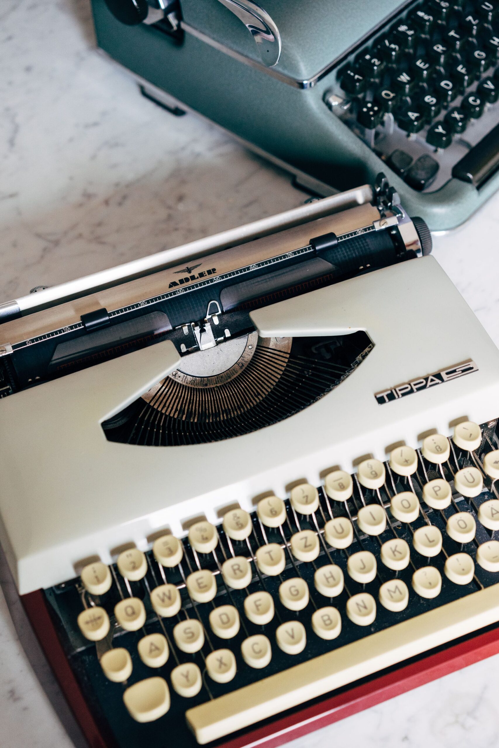 Two classic vintage typewriters on a marble surface, showcasing nostalgic technology.