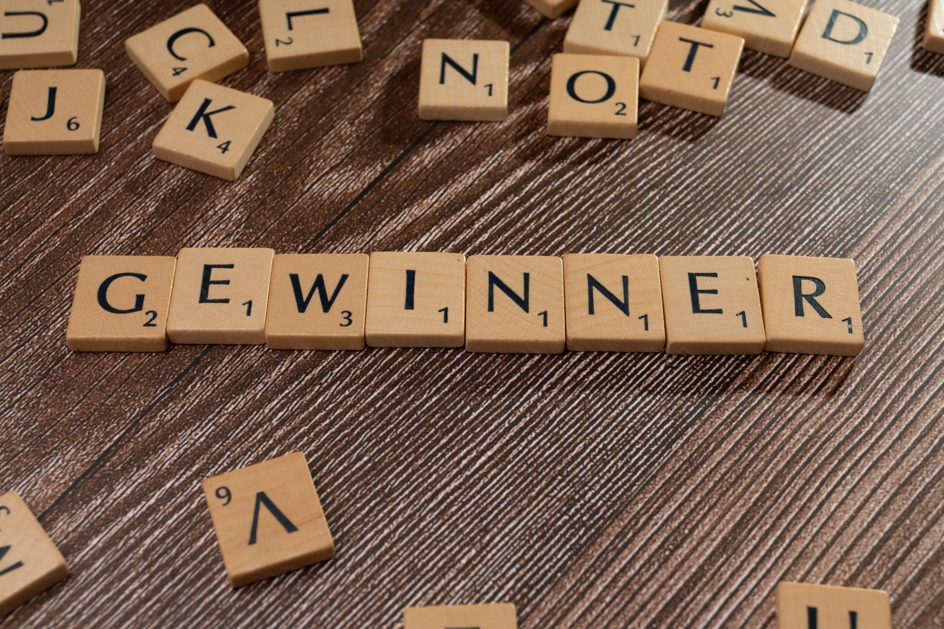 Scrabble tiles spelling the word Gewinner, meaning winner, on a wooden table
